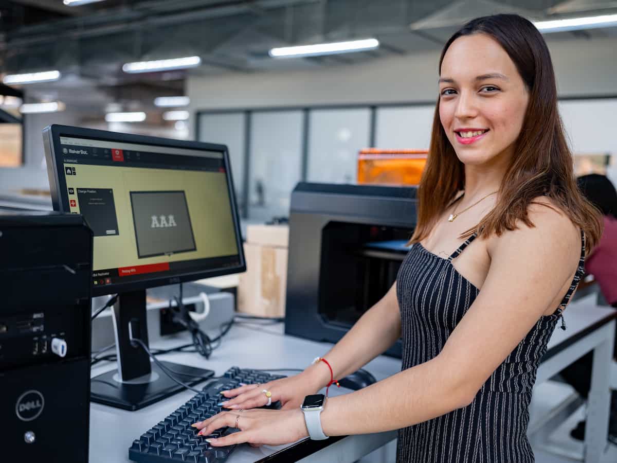 Estudiante sonriendo mientras trabaja con software de modelado 3D en un laboratorio de fabricación digital.