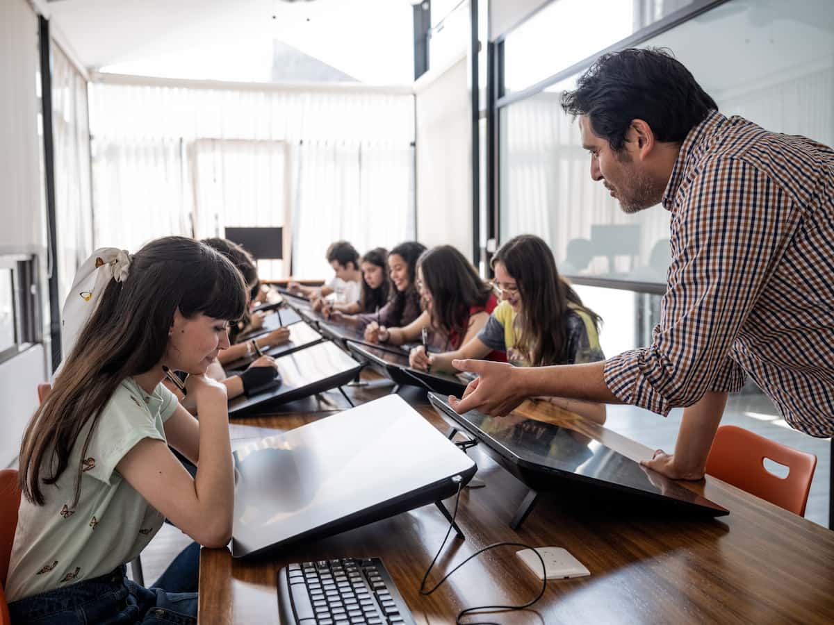 Joven diseñadora usando iMac en aula con rueda cromática sobre el escritorio, con logotipo de la Universidad Anáhuac al frente.