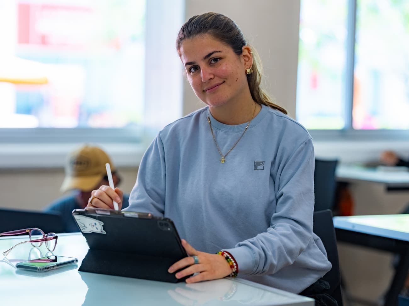 Estudiante concentrada escribiendo con lápiz digital sobre una tablet, en un espacio de estudio moderno dentro del campus Anáhuac.