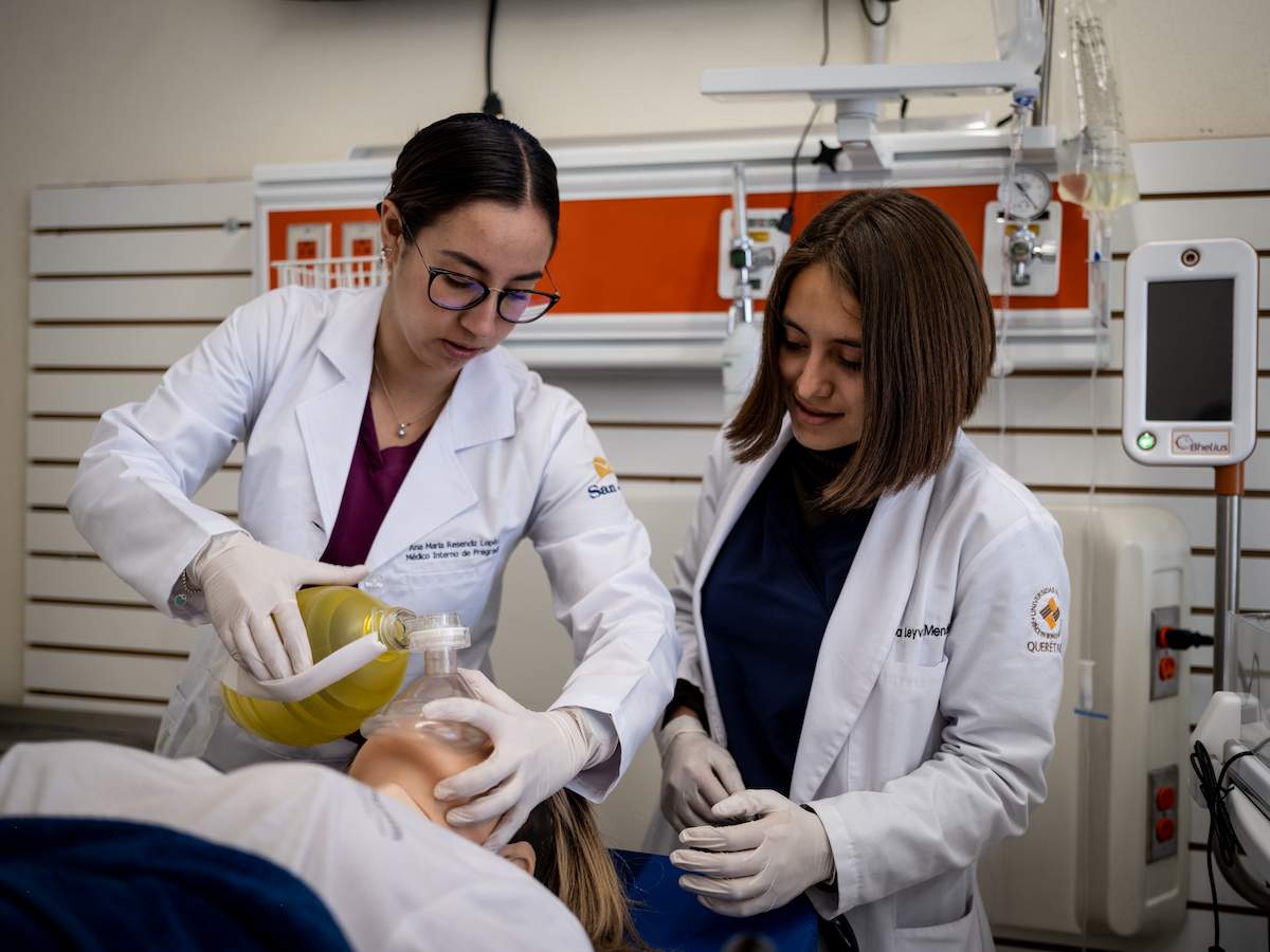 Dos estudiantes de medicina practican ventilación con ambú en un maniquí médico en un entorno clínico simulado.