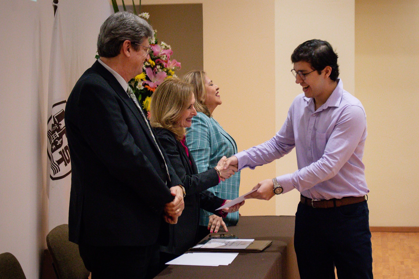 Alumno recibe reconocimiento de la Rectora. El Vicerrector Académico observa.