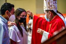Obispo confirmando a una adolescente en compañía de su padrino.