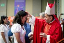 El obispo coloca la mano en la frente a la alumna confirmada.